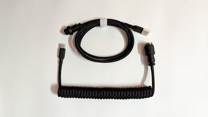 A coiled keyboard cable with black connectors on both ends. The cable is black and has a braided design.