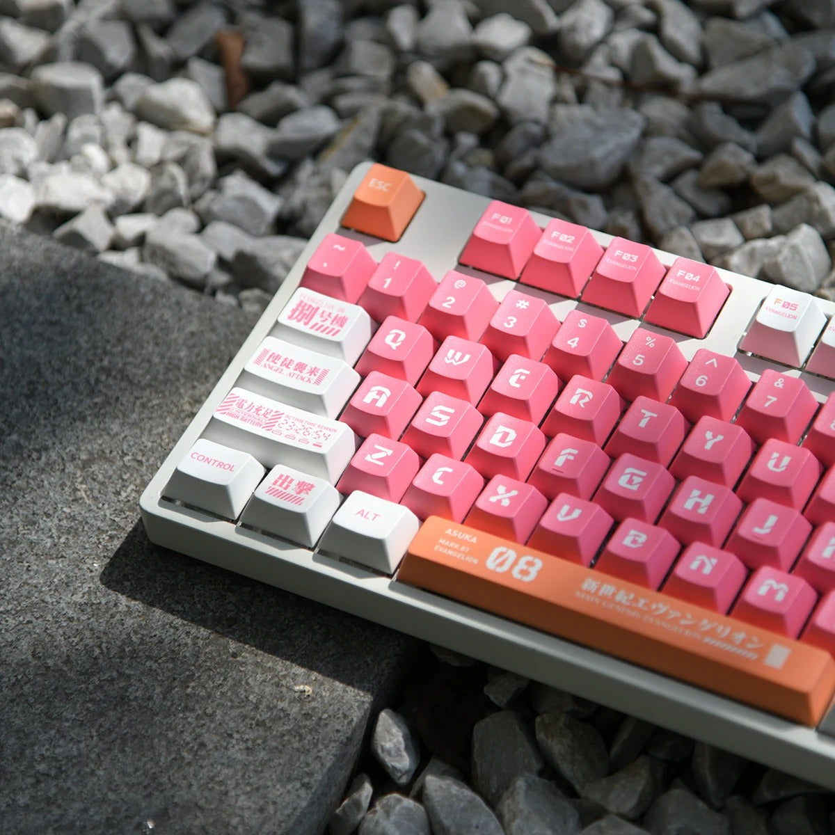 A close-up image of a mechanical keyboard featuring the Eva-08 Keycap Set. The keycaps are pink and white with Japanese characters and symbols. The keyboard is resting on a bed of small rocks.