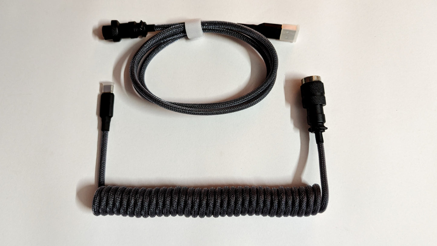 A coiled keyboard cable with gray connectors on both ends. The cable is gray and has a braided design.