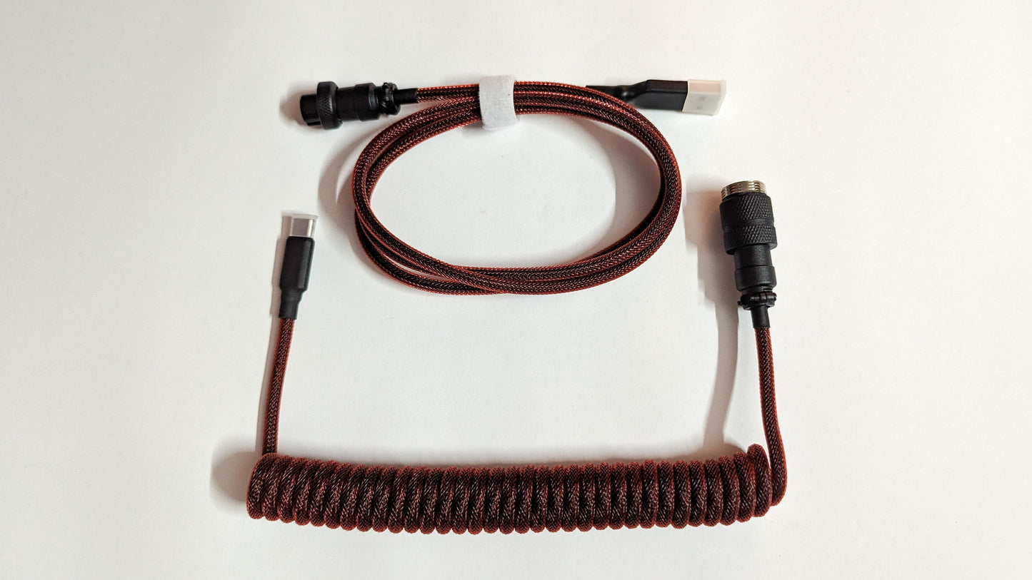 A coiled keyboard cable with maroon connectors on both ends. The cable is maroon and has a braided design.