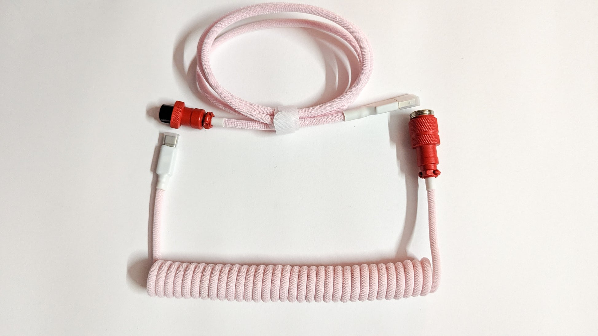 A coiled keyboard cable with pink connectors on both ends. The cable is pink and has a braided design.