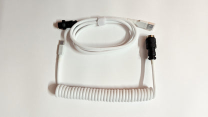 A coiled keyboard cable with white connectors on both ends. The cable is white and has a braided design.